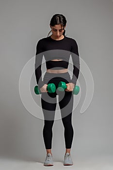 Focused girl ready to do exercises with dumbbells on grey background