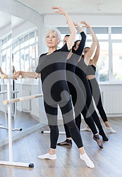 Elderly lady mastering battement tendu at barre during ballet class photo