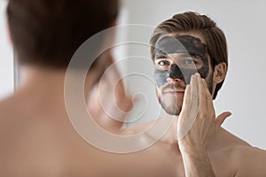 Focused handsome metrosexual guy applying dark cleansing natural clay photo