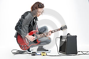 Focused handsome young guitarist playing electric guitar with amplifier