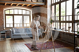 Focused happy old senior retired woman drawing on easel.