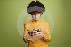 Focused Hispanic man using smartphone near green background