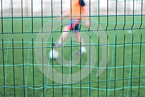 Focused image of sectional green fence. Soccer players with a ball plays on the background