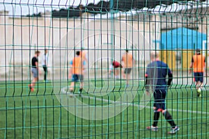 Focused image of sectional green fence. Soccer players with a ball plays on the background