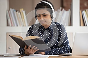 Focused indian girl in headphones studying reading book