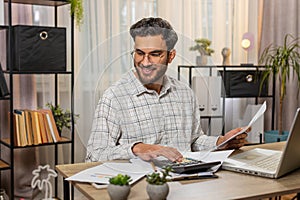 Focused Indian office worker working with schedules and financial graphics while using calculator