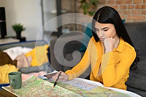 Focused lady planning future journey with map, choosing best travel routes and preparing for trip at home
