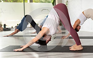 Focused Latin female practicing yoga pose Downward Facing Dog or Adho Mukha Svanasana in fitness gym group class