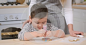 Focused little boy decorating homemade gingerbread cookie with colorful icing ay kitchen, close up, slow motion