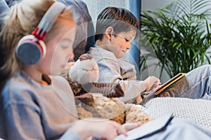 Focused little boy and girl in headphones using digital tablets