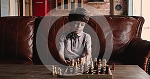 Focused little cute kid boy playing chess alone at home.