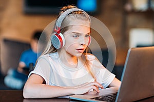 Focused little girl in headphones using laptop