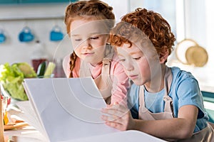 focused little kids reading cookbook while cooking together