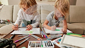 Focused little siblings, boy and girl drawing on paper using marker pen while spending time together at home