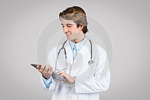 Focused male doctor using digital tablet on grey background