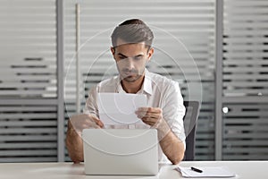 Focused male employee reading paper correspondence letter at workplace photo