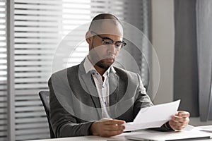 Focused male employee reading paper letter at workplace