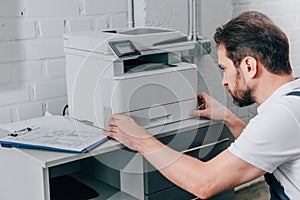 Focused male handyman repairing copy machine photo