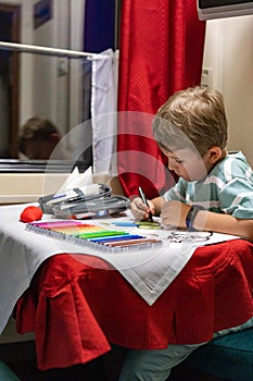 Focused male kid drawing writing paper notes enjoying travel by train at luxury railway carriage