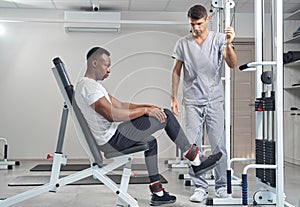 Focused male patient doing strength training exercise supervised by physiatrist