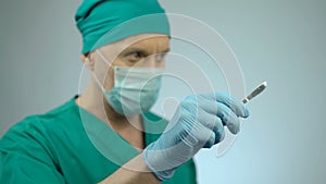 Focused male surgeon holding sharp scalpel in hand, nodding to start surgery