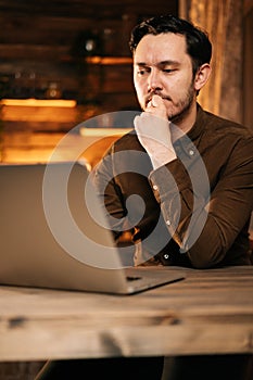 Focused man in casual clothing typing on laptop while sitting at the table.
