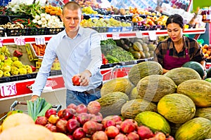 Focused man choosing pomegranates on counter in greengrocery store