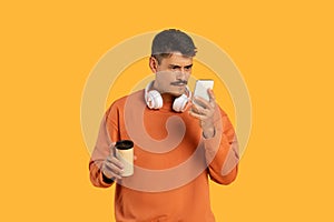 Focused man examining smartphone with coffee in hand