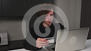 Focused man holding credit card, writing payment document, using laptop for online shopping. Man doing financial