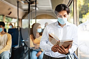 Focused man in mask reading book going by autobus