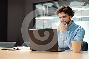 Focused man using laptop sitting at desk in office