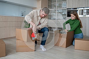 Focused man using tape packing cardboard boxes prepare to move with loving woman in new apartment