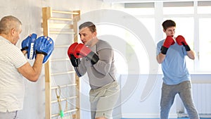 Focused man wearing boxing gloves working out with older male partner during self-defense course, practicing punches on