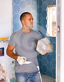 Focused man wearing ordinary clothes installing ceramic tiles whith construction trowel