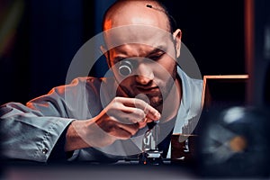 Focused man is working at his workshop with monocle and other tools repairing old watches