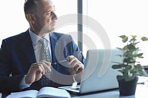 Focused mature businessman deep in thought while sitting at a table in modern office photo