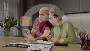 Focused mature couple with tablet pc managing household finance indoors