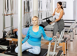Focused mature female in activewear training upper back while using Pilates performer bed in studio