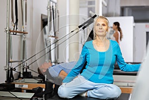Focused mature female in activewear training upper back while using Pilates performer bed in studio