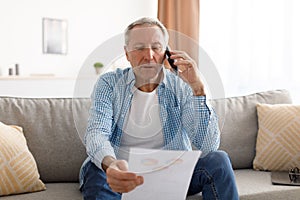 Focused mature man holding paper reading report talking on phone