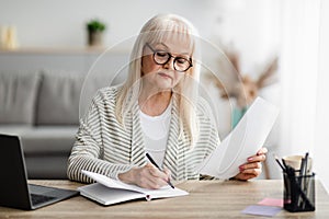 Focused mature woman writing and holding document at home