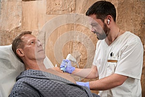 Focused medical specialist carefully using shockwave therapy on his male patient