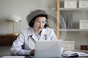 Focused mid adult general practitioner woman in headphones giving consultation