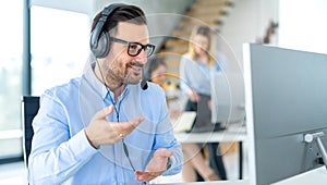 Focused middle aged handsome man in formal shirt and headset working on computer in call center agency.