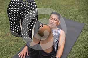 A focused middle aged male does a set of reverse crunches while lying on mat outdoors. Focus on foot sole