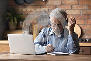 Focused middle aged man in headphones studying on online courses.