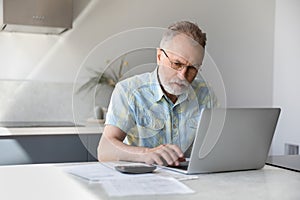 Focused middle aged retired man calculating budget.
