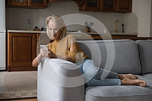 Focused middle aged senior lady using smartphone et home