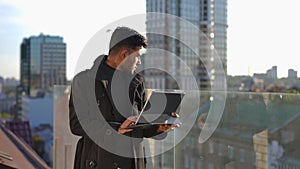 Focused Middle Eastern smart young man surfing Internet on tablet standing at background of urban city. Portrait of