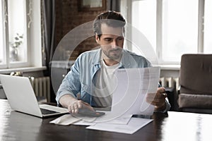 Focused millennial man paying domestic bills, using calculator